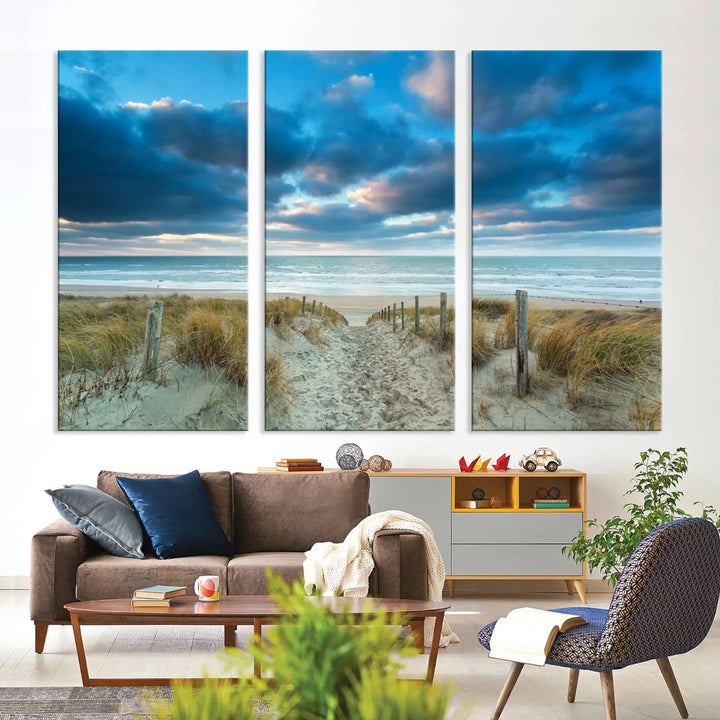 The "Beach Ocean Sun Sand Wall Art Canvas Print" is a triptych showcasing a beach path with grass leading to the ocean under a dramatic cloudy sky. This museum-quality canvas includes a UV-protective coating for longevity and vibrancy, and it comes ready to hang for effortless elegance.