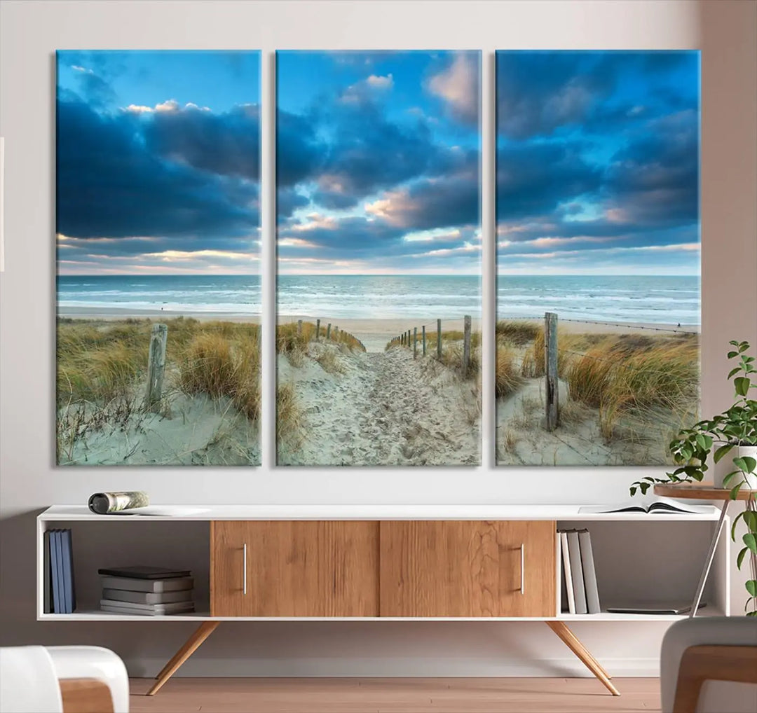 The "Beach Ocean Sun Sand Wall Art Canvas Print" is a triptych showcasing a beach path with grass leading to the ocean under a dramatic cloudy sky. This museum-quality canvas includes a UV-protective coating for longevity and vibrancy, and it comes ready to hang for effortless elegance.