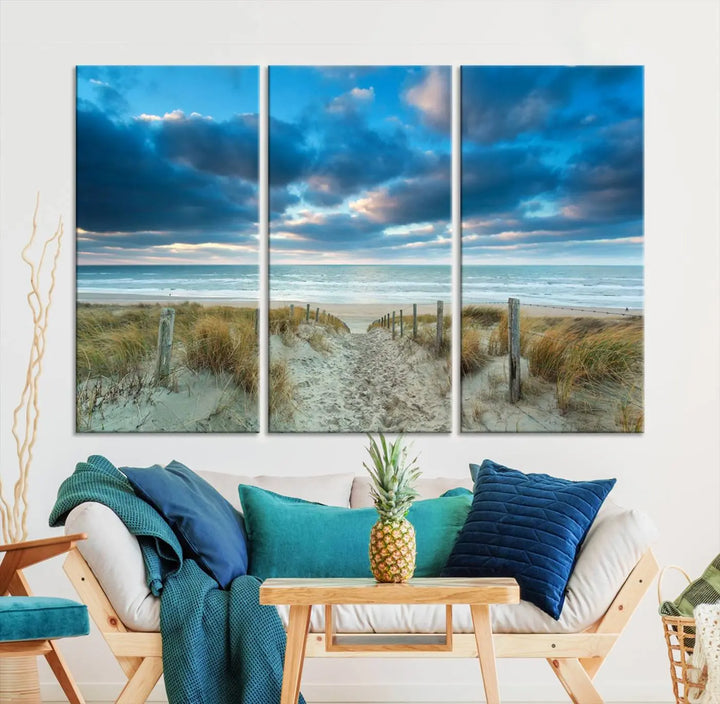 The "Beach Ocean Sun Sand Wall Art Canvas Print" is a triptych showcasing a beach path with grass leading to the ocean under a dramatic cloudy sky. This museum-quality canvas includes a UV-protective coating for longevity and vibrancy, and it comes ready to hang for effortless elegance.