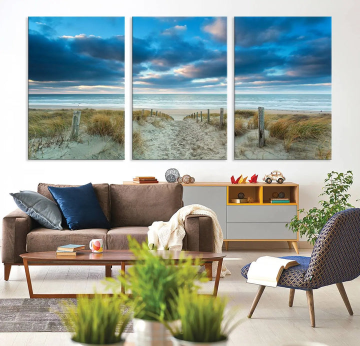 The "Beach Ocean Sun Sand Wall Art Canvas Print" is a triptych showcasing a beach path with grass leading to the ocean under a dramatic cloudy sky. This museum-quality canvas includes a UV-protective coating for longevity and vibrancy, and it comes ready to hang for effortless elegance.