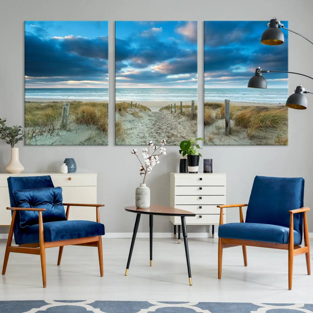 The "Beach Ocean Sun Sand Wall Art Canvas Print" is a triptych showcasing a beach path with grass leading to the ocean under a dramatic cloudy sky. This museum-quality canvas includes a UV-protective coating for longevity and vibrancy, and it comes ready to hang for effortless elegance.