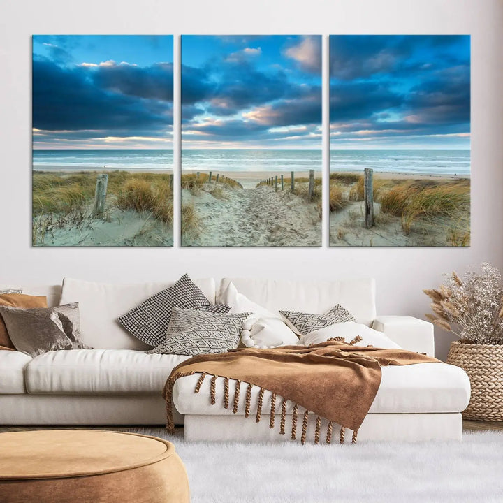 The "Beach Ocean Sun Sand Wall Art Canvas Print" is a triptych showcasing a beach path with grass leading to the ocean under a dramatic cloudy sky. This museum-quality canvas includes a UV-protective coating for longevity and vibrancy, and it comes ready to hang for effortless elegance.