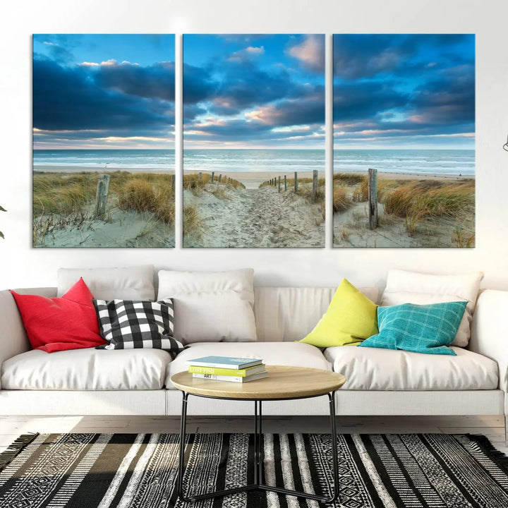 The "Beach Ocean Sun Sand Wall Art Canvas Print" is a triptych showcasing a beach path with grass leading to the ocean under a dramatic cloudy sky. This museum-quality canvas includes a UV-protective coating for longevity and vibrancy, and it comes ready to hang for effortless elegance.