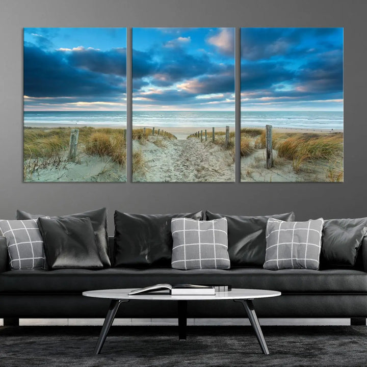 The "Beach Ocean Sun Sand Wall Art Canvas Print" is a triptych showcasing a beach path with grass leading to the ocean under a dramatic cloudy sky. This museum-quality canvas includes a UV-protective coating for longevity and vibrancy, and it comes ready to hang for effortless elegance.