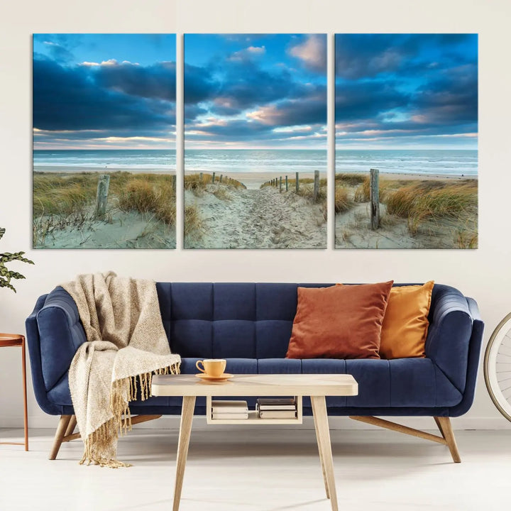 The "Beach Ocean Sun Sand Wall Art Canvas Print" is a triptych showcasing a beach path with grass leading to the ocean under a dramatic cloudy sky. This museum-quality canvas includes a UV-protective coating for longevity and vibrancy, and it comes ready to hang for effortless elegance.