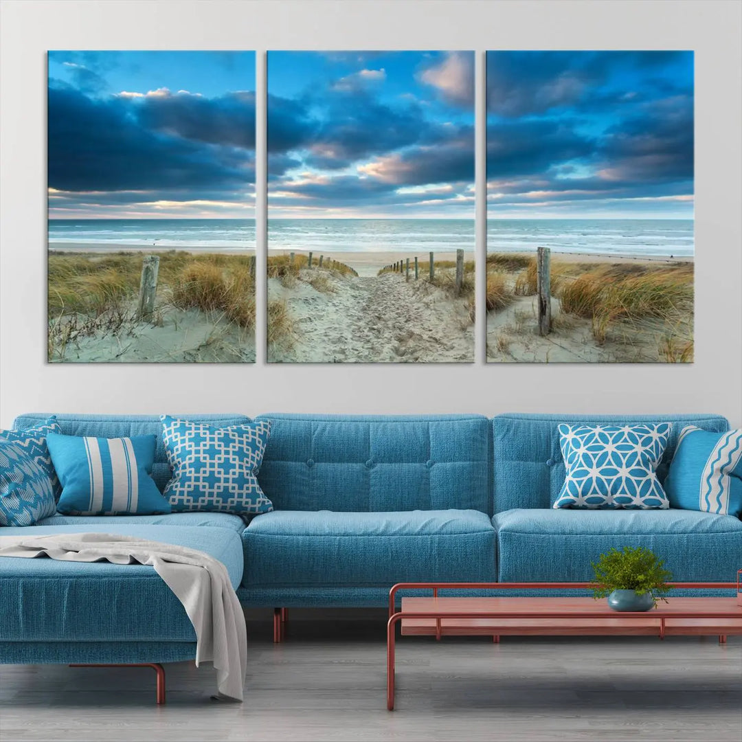 The "Beach Ocean Sun Sand Wall Art Canvas Print" is a triptych showcasing a beach path with grass leading to the ocean under a dramatic cloudy sky. This museum-quality canvas includes a UV-protective coating for longevity and vibrancy, and it comes ready to hang for effortless elegance.