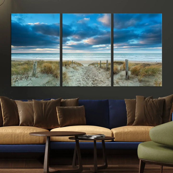 The "Beach Ocean Sun Sand Wall Art Canvas Print" is a triptych showcasing a beach path with grass leading to the ocean under a dramatic cloudy sky. This museum-quality canvas includes a UV-protective coating for longevity and vibrancy, and it comes ready to hang for effortless elegance.