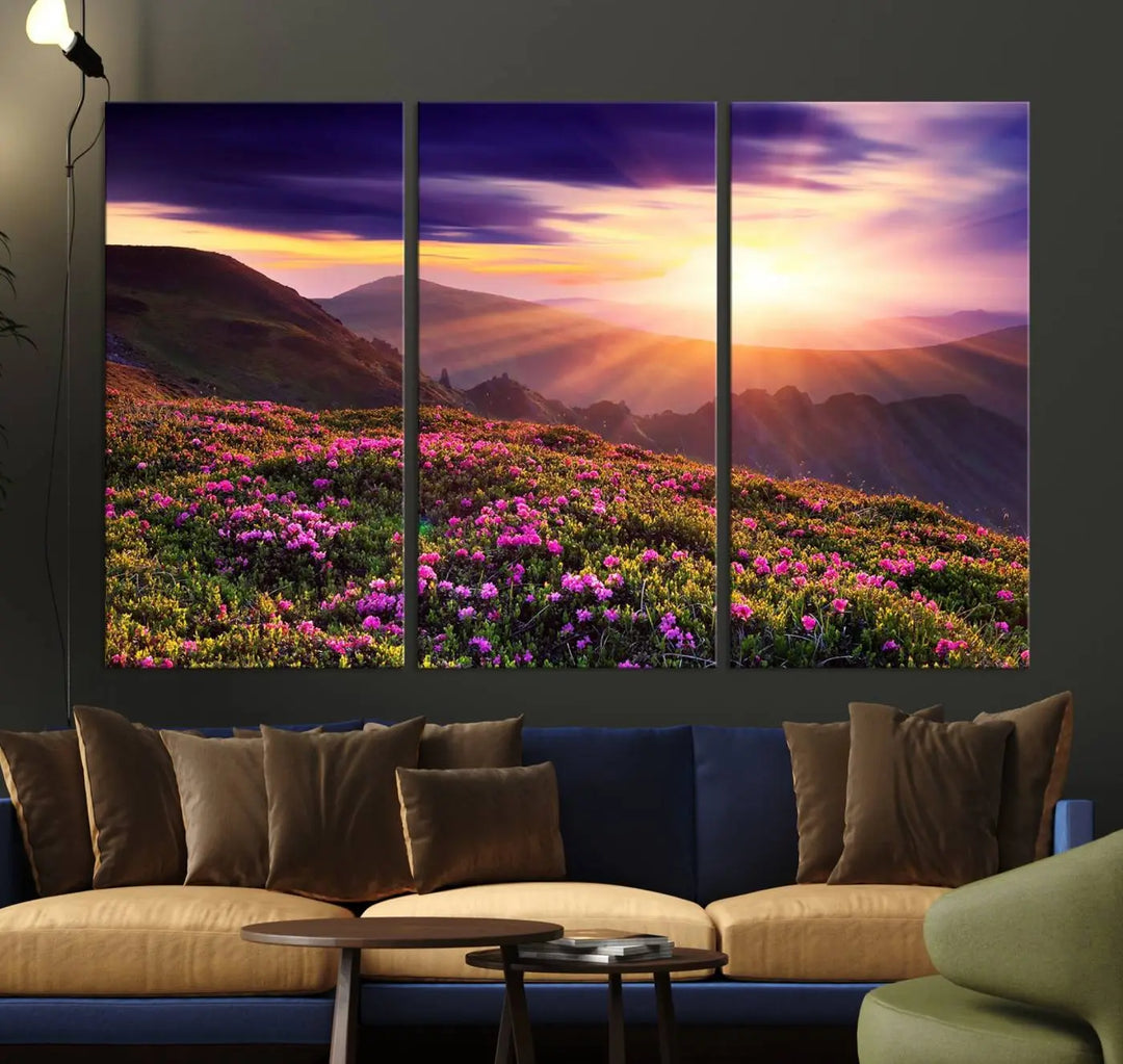 A living room showcases the Beautiful Mountain Sunset Landscape with Purple Flowers Canvas Wall Art Print, featuring a triptych of a vibrant sunset over mountains and blooming flowers, vividly rendered on museum-quality canvas with UV-protective coating.