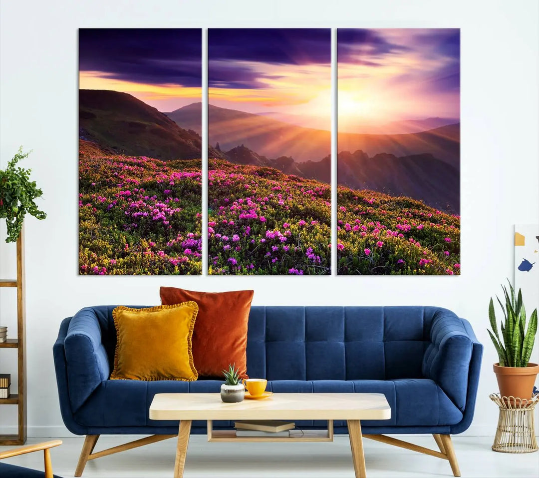 A living room showcases the Beautiful Mountain Sunset Landscape with Purple Flowers Canvas Wall Art Print, featuring a triptych of a vibrant sunset over mountains and blooming flowers, vividly rendered on museum-quality canvas with UV-protective coating.