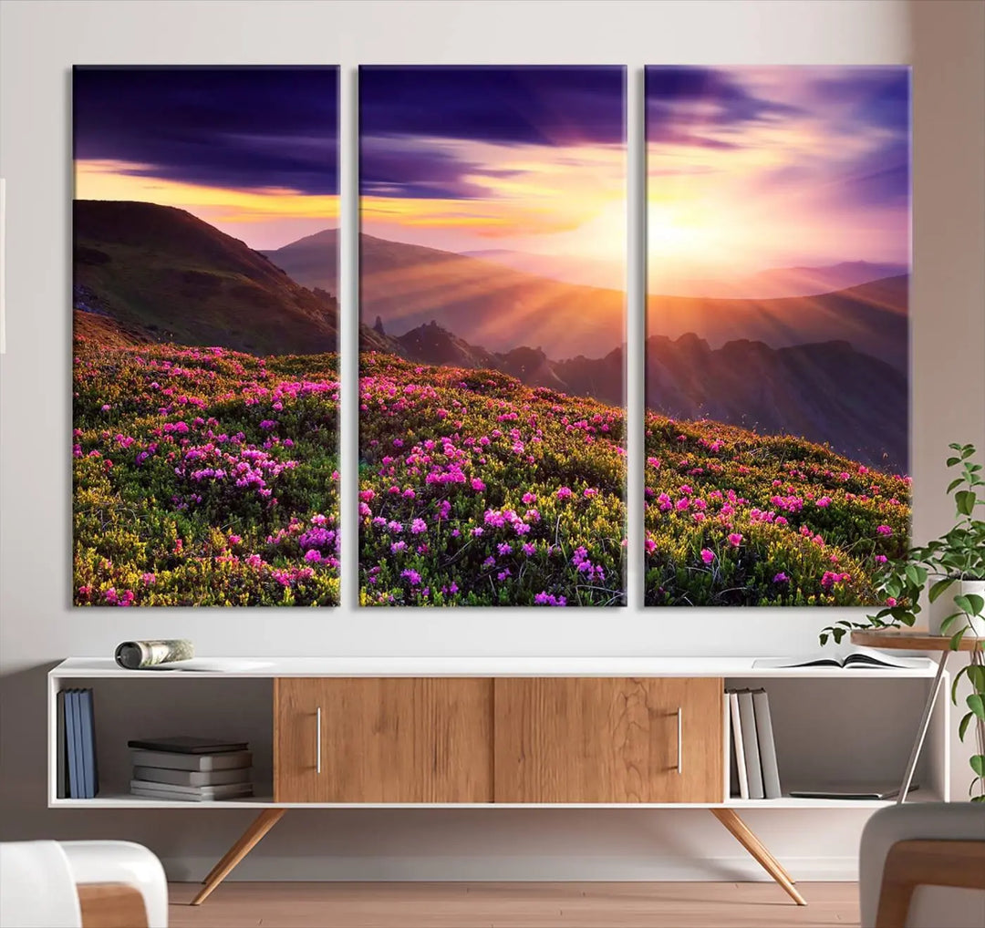 A living room showcases the Beautiful Mountain Sunset Landscape with Purple Flowers Canvas Wall Art Print, featuring a triptych of a vibrant sunset over mountains and blooming flowers, vividly rendered on museum-quality canvas with UV-protective coating.