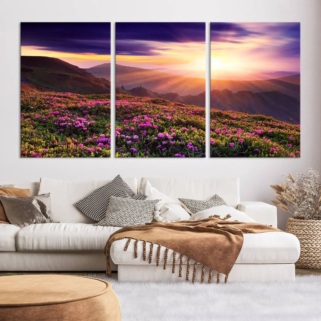 A living room showcases the Beautiful Mountain Sunset Landscape with Purple Flowers Canvas Wall Art Print, featuring a triptych of a vibrant sunset over mountains and blooming flowers, vividly rendered on museum-quality canvas with UV-protective coating.