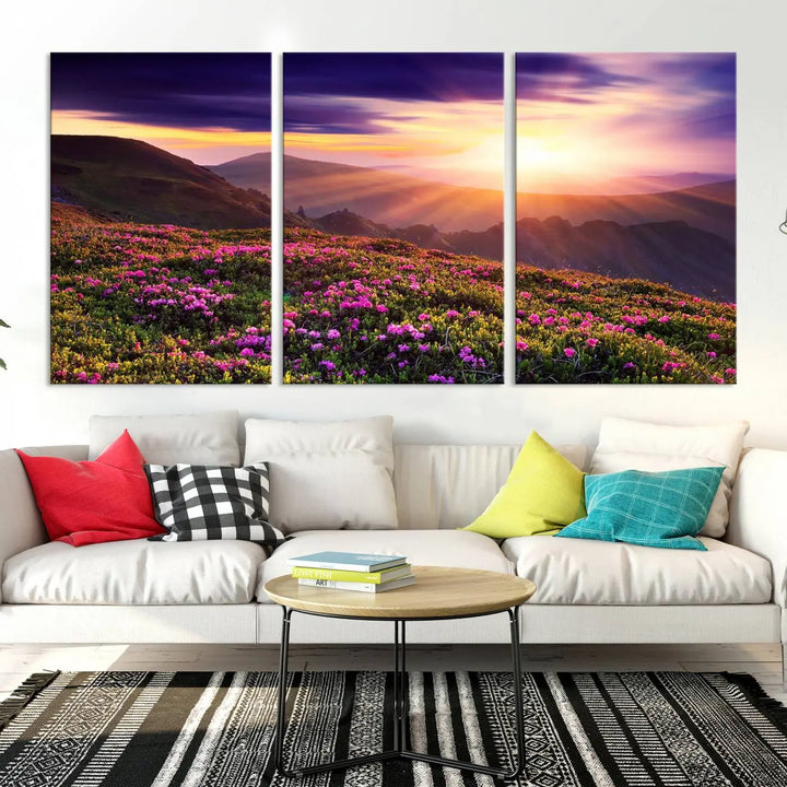 A living room showcases the Beautiful Mountain Sunset Landscape with Purple Flowers Canvas Wall Art Print, featuring a triptych of a vibrant sunset over mountains and blooming flowers, vividly rendered on museum-quality canvas with UV-protective coating.