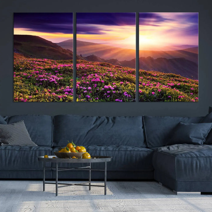 A living room showcases the Beautiful Mountain Sunset Landscape with Purple Flowers Canvas Wall Art Print, featuring a triptych of a vibrant sunset over mountains and blooming flowers, vividly rendered on museum-quality canvas with UV-protective coating.