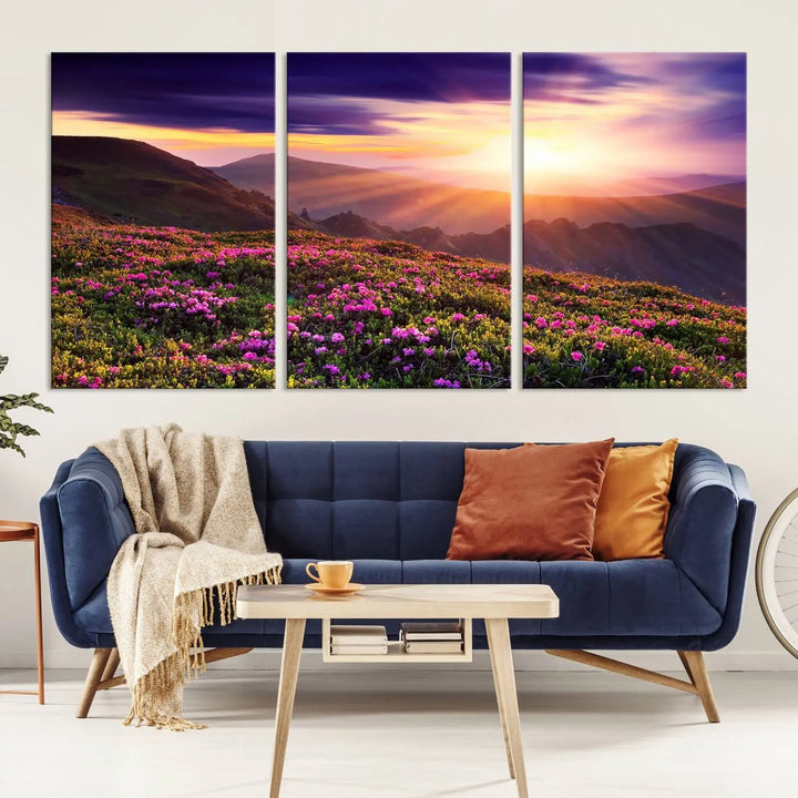 A living room showcases the Beautiful Mountain Sunset Landscape with Purple Flowers Canvas Wall Art Print, featuring a triptych of a vibrant sunset over mountains and blooming flowers, vividly rendered on museum-quality canvas with UV-protective coating.