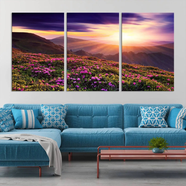 A living room showcases the Beautiful Mountain Sunset Landscape with Purple Flowers Canvas Wall Art Print, featuring a triptych of a vibrant sunset over mountains and blooming flowers, vividly rendered on museum-quality canvas with UV-protective coating.