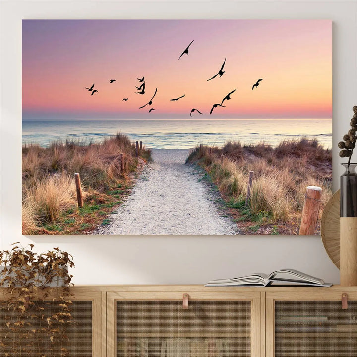 The "Birds on the Beach Sunset Wall Art Canvas Print" showcases a serene scene of seagulls soaring over a beach path at sunrise, beautifully capturing the endless sea and sky.