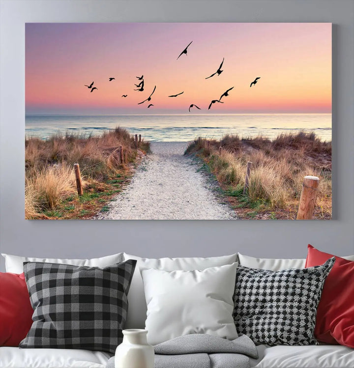 The "Birds on the Beach Sunset Wall Art Canvas Print" showcases a serene scene of seagulls soaring over a beach path at sunrise, beautifully capturing the endless sea and sky.