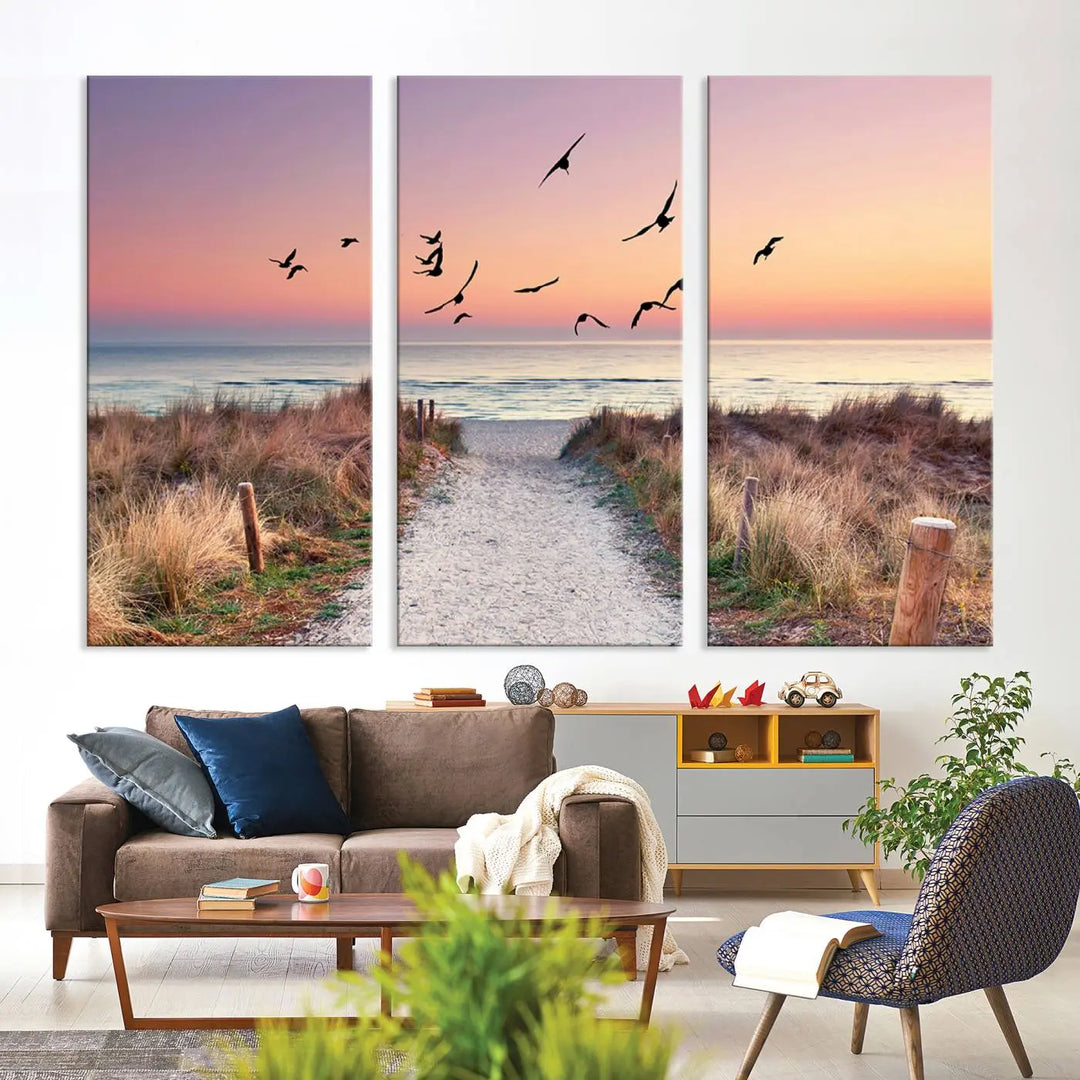 The "Birds on the Beach Sunset Wall Art Canvas Print" showcases a serene scene of seagulls soaring over a beach path at sunrise, beautifully capturing the endless sea and sky.