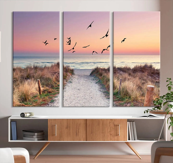 The "Birds on the Beach Sunset Wall Art Canvas Print" showcases a serene scene of seagulls soaring over a beach path at sunrise, beautifully capturing the endless sea and sky.