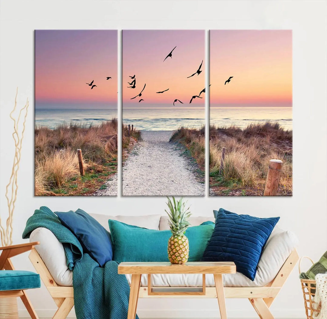 The "Birds on the Beach Sunset Wall Art Canvas Print" showcases a serene scene of seagulls soaring over a beach path at sunrise, beautifully capturing the endless sea and sky.