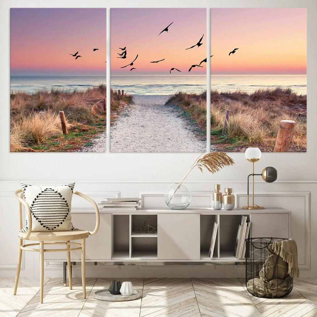 The "Birds on the Beach Sunset Wall Art Canvas Print" showcases a serene scene of seagulls soaring over a beach path at sunrise, beautifully capturing the endless sea and sky.