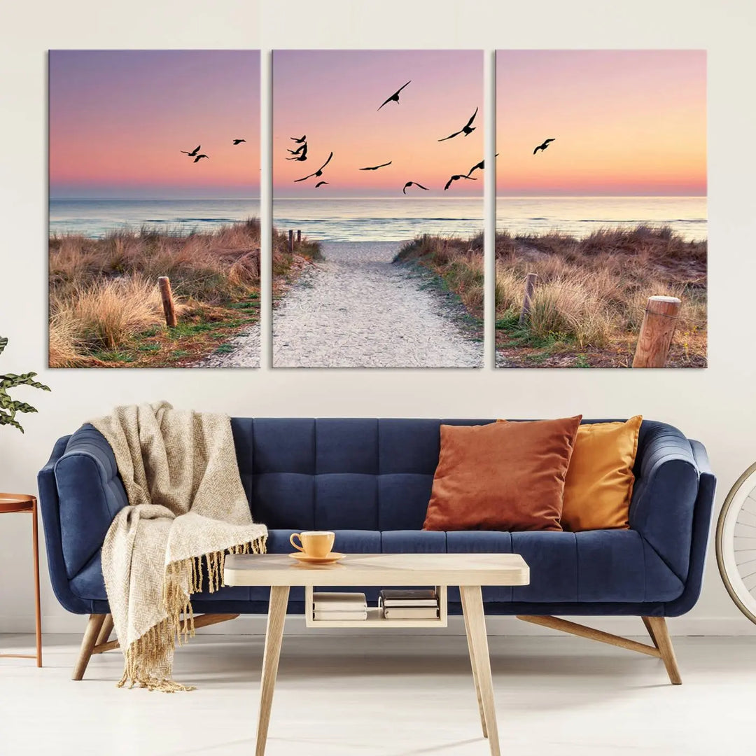 The "Birds on the Beach Sunset Wall Art Canvas Print" showcases a serene scene of seagulls soaring over a beach path at sunrise, beautifully capturing the endless sea and sky.