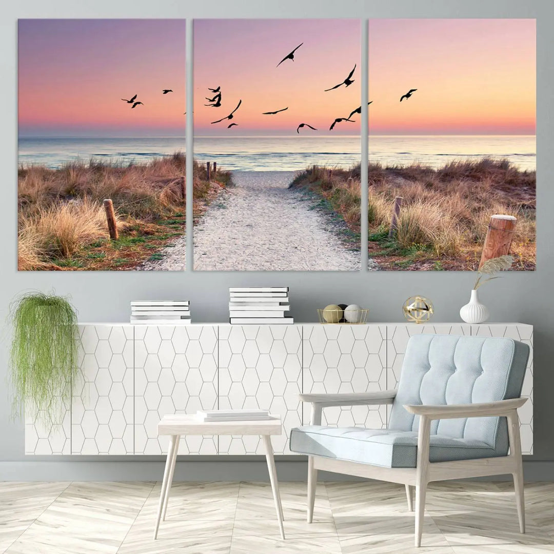 The "Birds on the Beach Sunset Wall Art Canvas Print" showcases a serene scene of seagulls soaring over a beach path at sunrise, beautifully capturing the endless sea and sky.