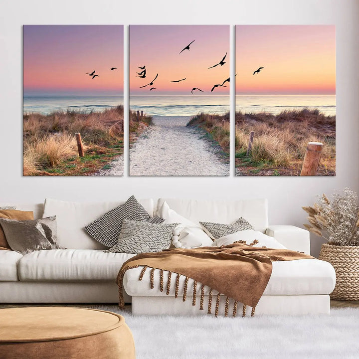 The "Birds on the Beach Sunset Wall Art Canvas Print" showcases a serene scene of seagulls soaring over a beach path at sunrise, beautifully capturing the endless sea and sky.