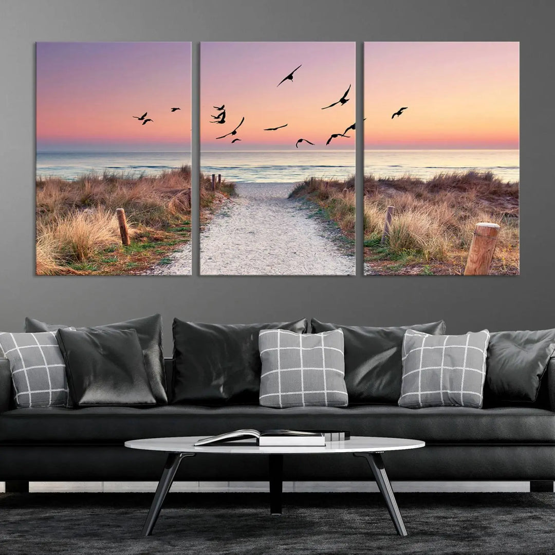 The "Birds on the Beach Sunset Wall Art Canvas Print" showcases a serene scene of seagulls soaring over a beach path at sunrise, beautifully capturing the endless sea and sky.