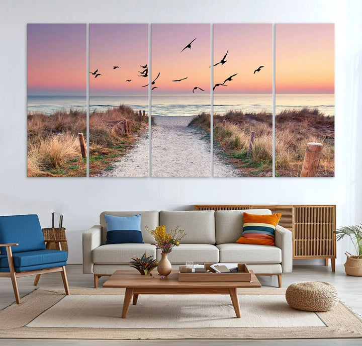 The "Birds on the Beach Sunset Wall Art Canvas Print" showcases a serene scene of seagulls soaring over a beach path at sunrise, beautifully capturing the endless sea and sky.