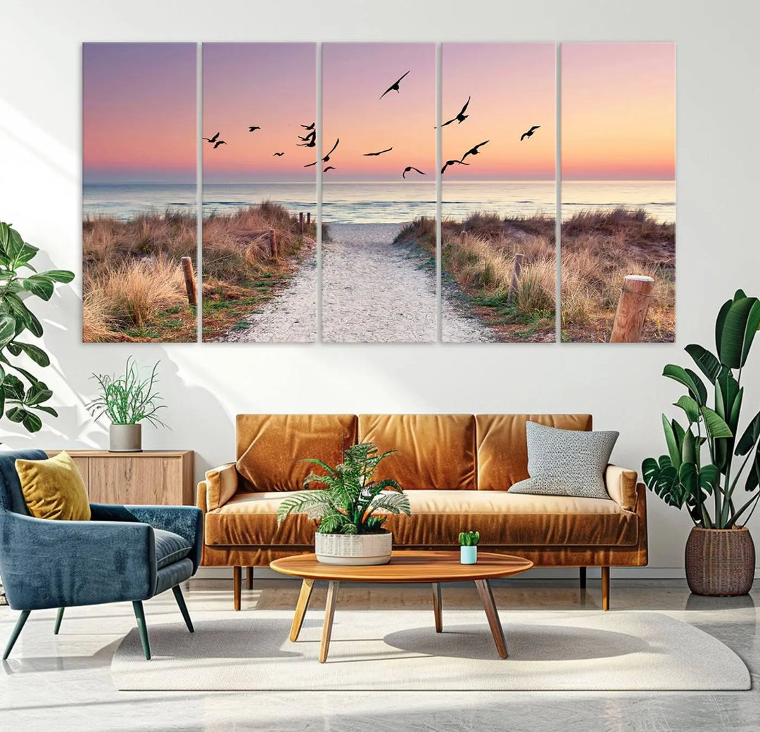 The "Birds on the Beach Sunset Wall Art Canvas Print" showcases a serene scene of seagulls soaring over a beach path at sunrise, beautifully capturing the endless sea and sky.