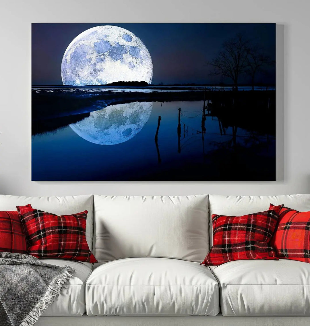 A mesmerizing Blue Moon Wall Art Canvas Print, depicting a lake landscape with a silhouetted tree, is beautifully presented on museum-quality canvas. This gallery-wrapped artwork, protected by a UV-coating to preserve its stunning details, stands out as an exquisite piece in the room.