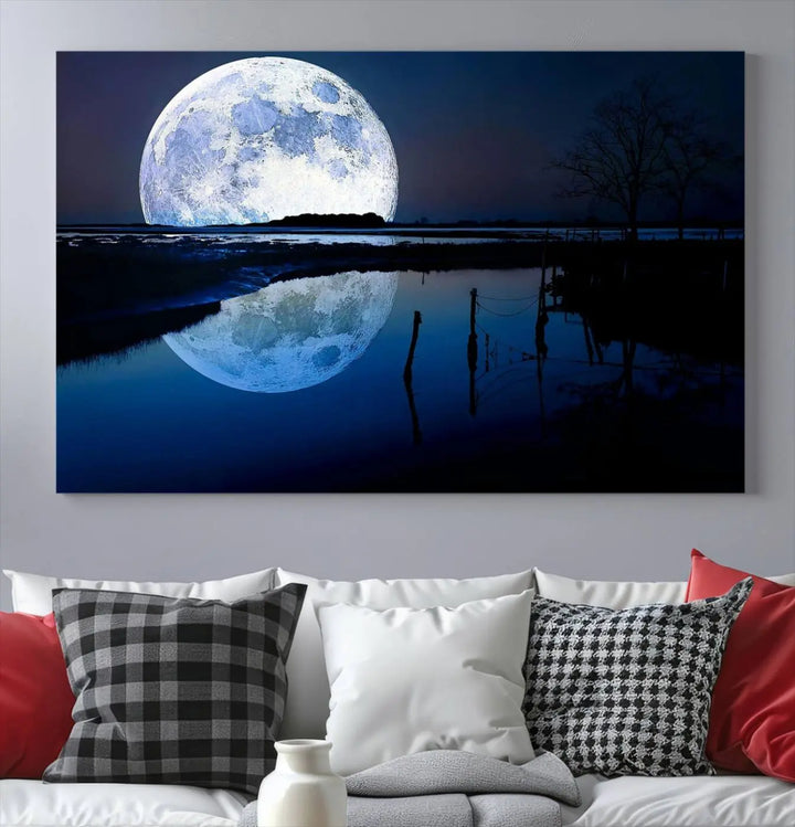 A mesmerizing Blue Moon Wall Art Canvas Print, depicting a lake landscape with a silhouetted tree, is beautifully presented on museum-quality canvas. This gallery-wrapped artwork, protected by a UV-coating to preserve its stunning details, stands out as an exquisite piece in the room.