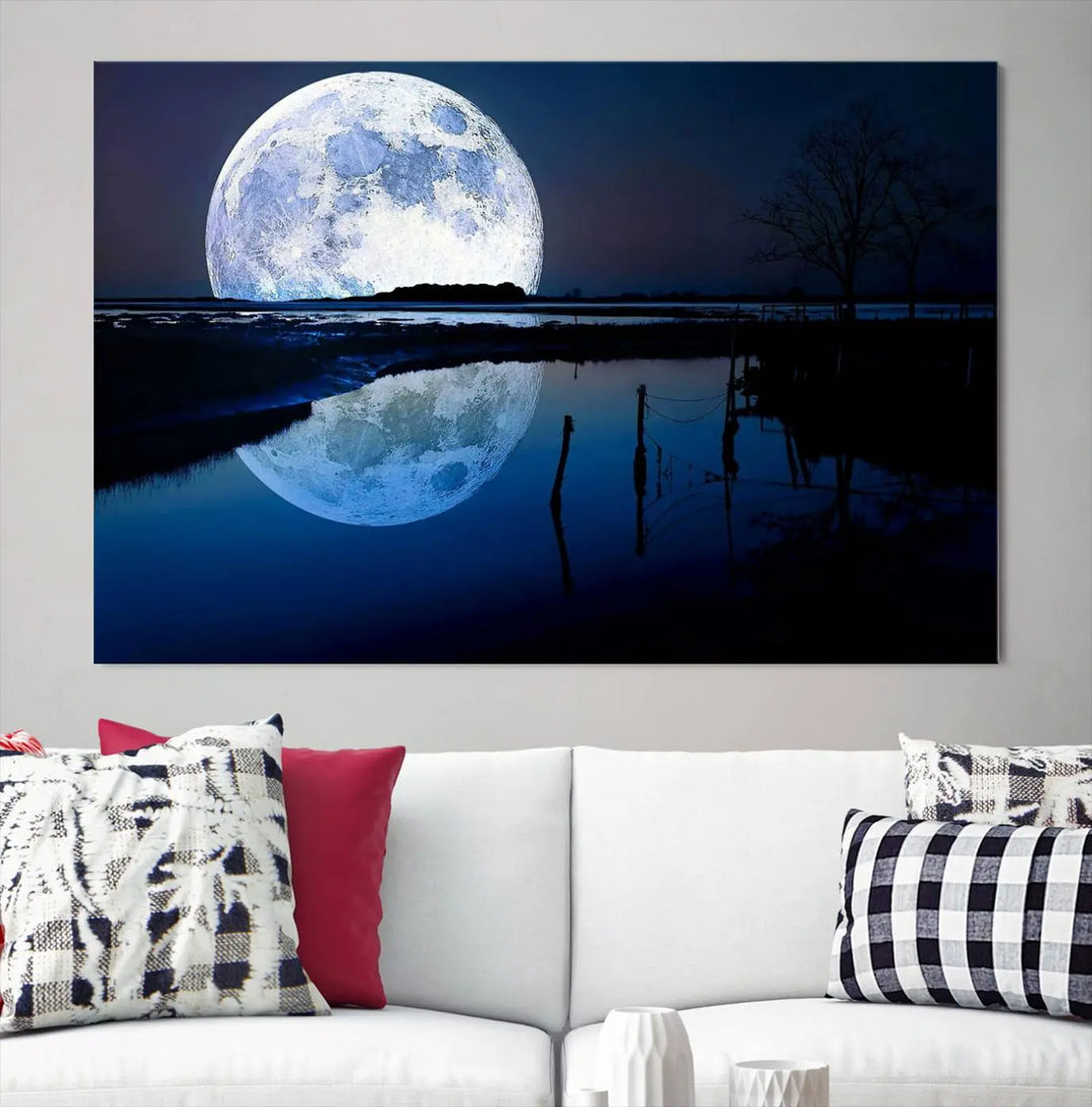 A mesmerizing Blue Moon Wall Art Canvas Print, depicting a lake landscape with a silhouetted tree, is beautifully presented on museum-quality canvas. This gallery-wrapped artwork, protected by a UV-coating to preserve its stunning details, stands out as an exquisite piece in the room.