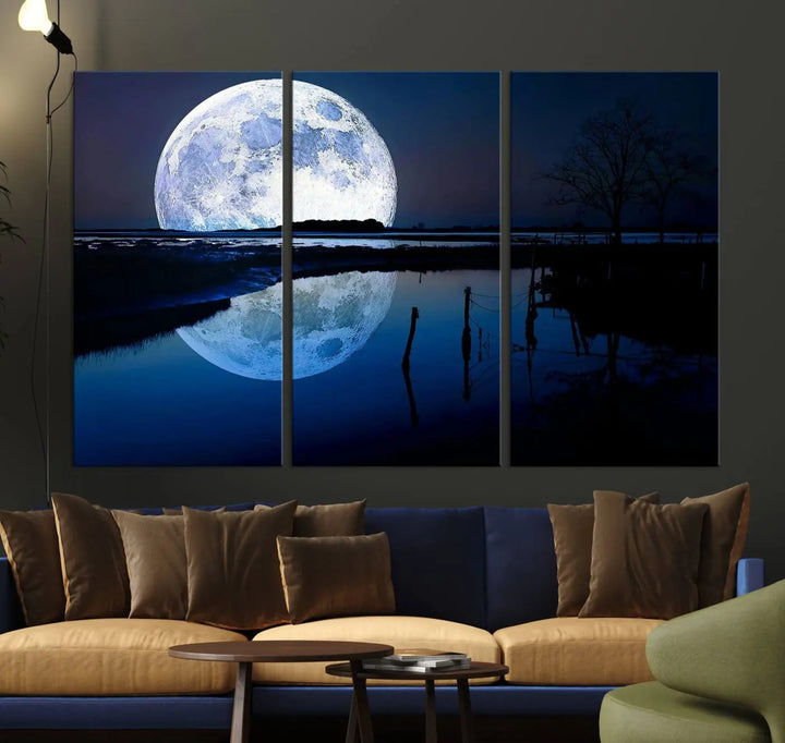 A mesmerizing Blue Moon Wall Art Canvas Print, depicting a lake landscape with a silhouetted tree, is beautifully presented on museum-quality canvas. This gallery-wrapped artwork, protected by a UV-coating to preserve its stunning details, stands out as an exquisite piece in the room.