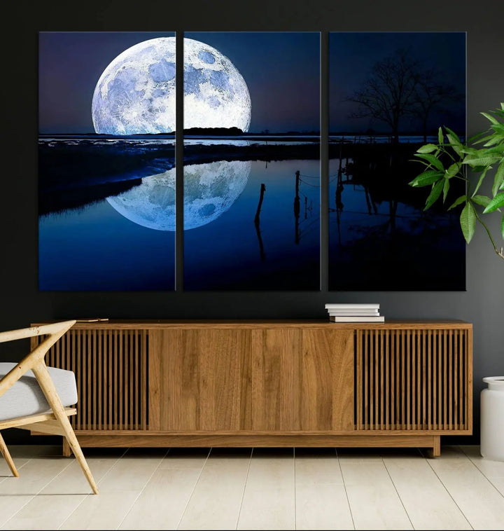 A mesmerizing Blue Moon Wall Art Canvas Print, depicting a lake landscape with a silhouetted tree, is beautifully presented on museum-quality canvas. This gallery-wrapped artwork, protected by a UV-coating to preserve its stunning details, stands out as an exquisite piece in the room.