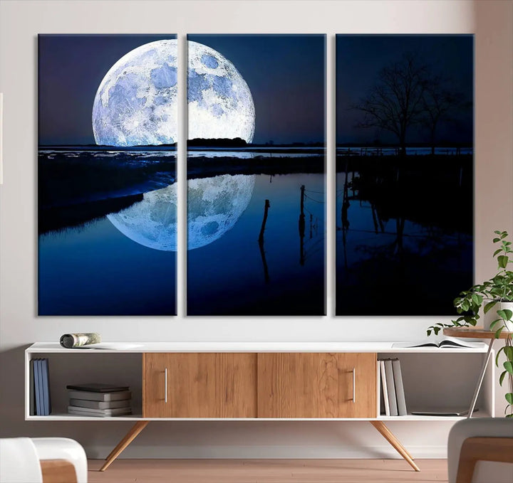 A mesmerizing Blue Moon Wall Art Canvas Print, depicting a lake landscape with a silhouetted tree, is beautifully presented on museum-quality canvas. This gallery-wrapped artwork, protected by a UV-coating to preserve its stunning details, stands out as an exquisite piece in the room.