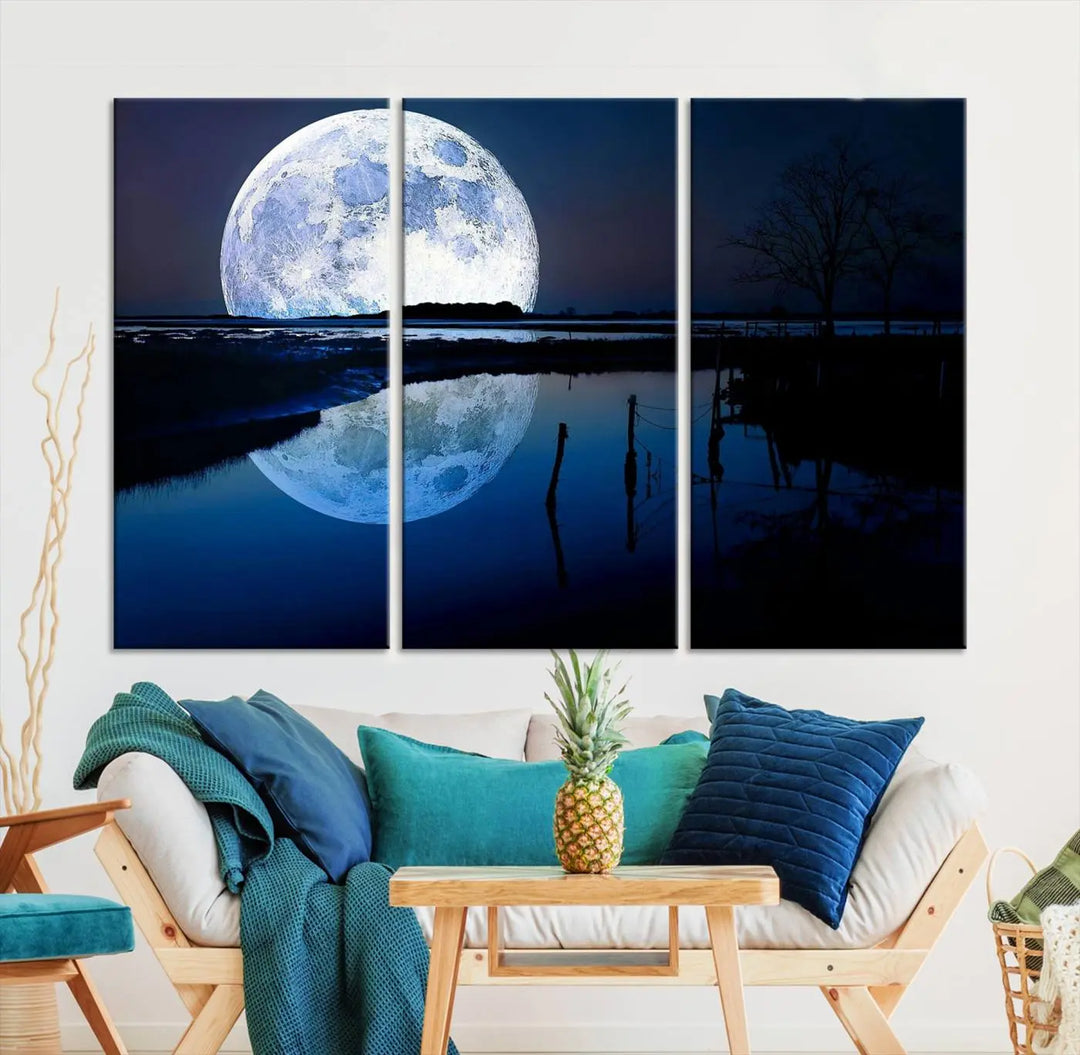 A mesmerizing Blue Moon Wall Art Canvas Print, depicting a lake landscape with a silhouetted tree, is beautifully presented on museum-quality canvas. This gallery-wrapped artwork, protected by a UV-coating to preserve its stunning details, stands out as an exquisite piece in the room.