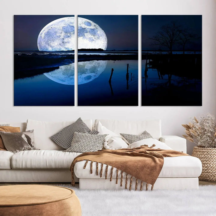 A mesmerizing Blue Moon Wall Art Canvas Print, depicting a lake landscape with a silhouetted tree, is beautifully presented on museum-quality canvas. This gallery-wrapped artwork, protected by a UV-coating to preserve its stunning details, stands out as an exquisite piece in the room.