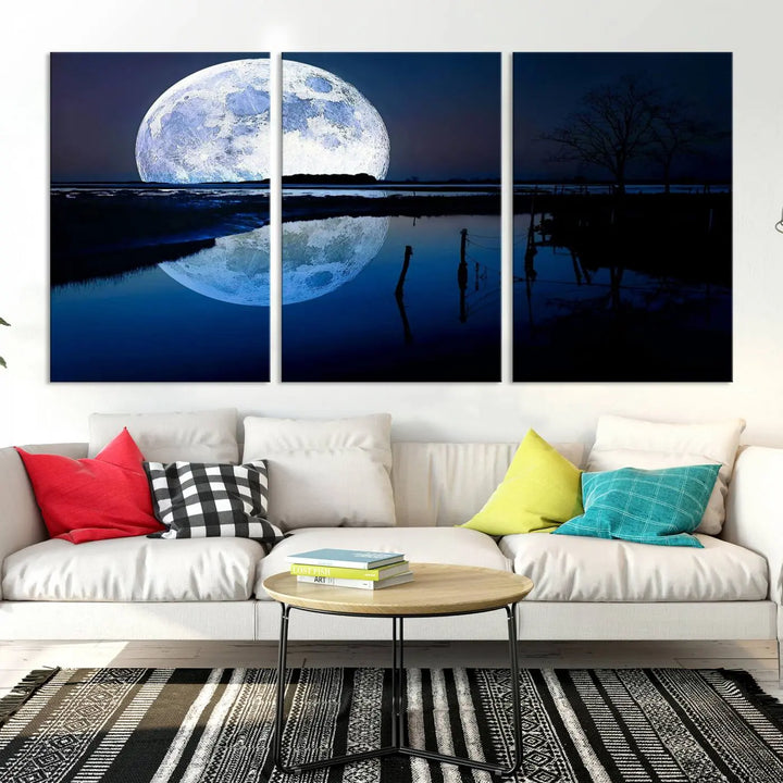 A mesmerizing Blue Moon Wall Art Canvas Print, depicting a lake landscape with a silhouetted tree, is beautifully presented on museum-quality canvas. This gallery-wrapped artwork, protected by a UV-coating to preserve its stunning details, stands out as an exquisite piece in the room.