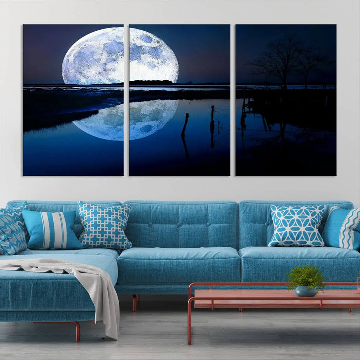 A mesmerizing Blue Moon Wall Art Canvas Print, depicting a lake landscape with a silhouetted tree, is beautifully presented on museum-quality canvas. This gallery-wrapped artwork, protected by a UV-coating to preserve its stunning details, stands out as an exquisite piece in the room.