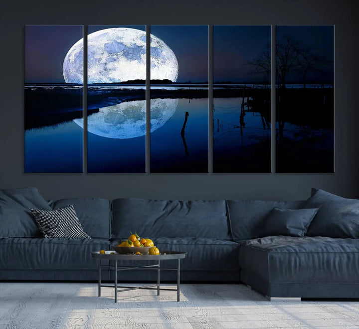 A mesmerizing Blue Moon Wall Art Canvas Print, depicting a lake landscape with a silhouetted tree, is beautifully presented on museum-quality canvas. This gallery-wrapped artwork, protected by a UV-coating to preserve its stunning details, stands out as an exquisite piece in the room.