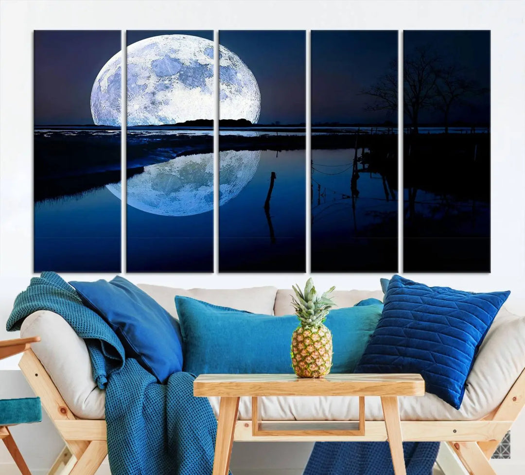 A mesmerizing Blue Moon Wall Art Canvas Print, depicting a lake landscape with a silhouetted tree, is beautifully presented on museum-quality canvas. This gallery-wrapped artwork, protected by a UV-coating to preserve its stunning details, stands out as an exquisite piece in the room.