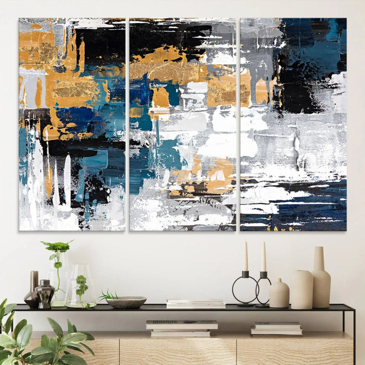 The Blue and Gold Abstract Canvas Wall Art – a triptych modern painting that's framed and ready to hang – features captivating brush strokes in blue, gold, black, and white to enhance the living room decor.