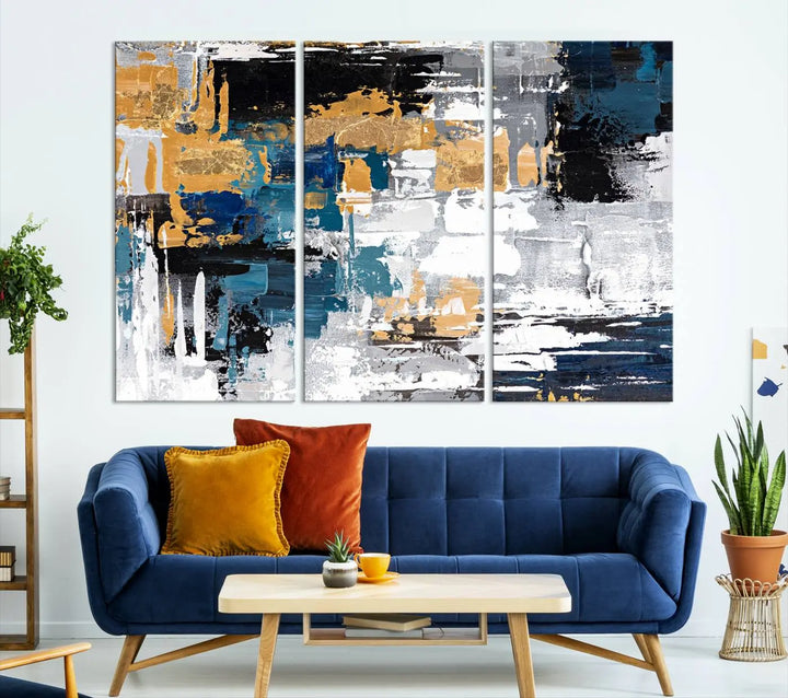 The Blue and Gold Abstract Canvas Wall Art – a triptych modern painting that's framed and ready to hang – features captivating brush strokes in blue, gold, black, and white to enhance the living room decor.