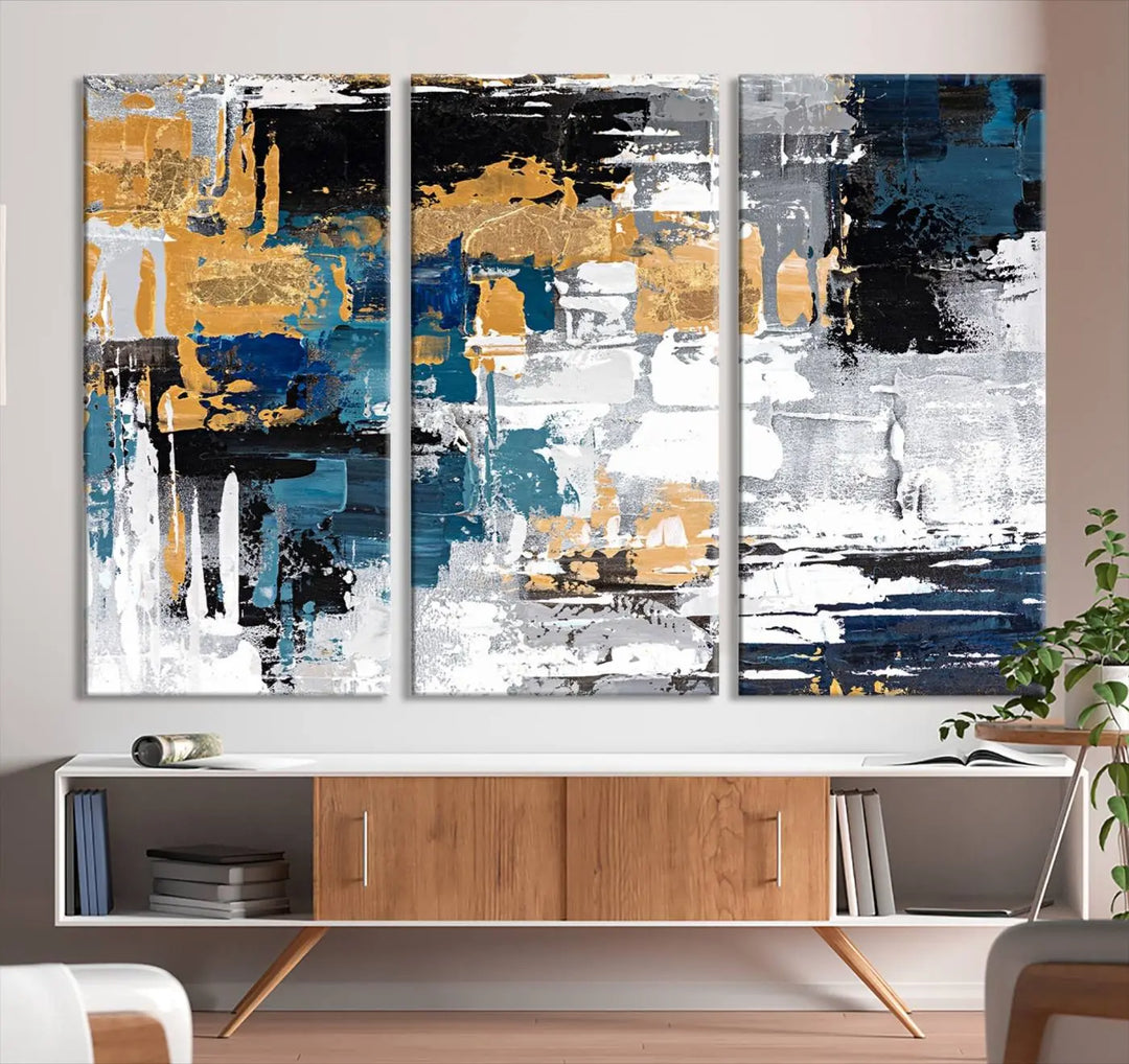 The Blue and Gold Abstract Canvas Wall Art – a triptych modern painting that's framed and ready to hang – features captivating brush strokes in blue, gold, black, and white to enhance the living room decor.