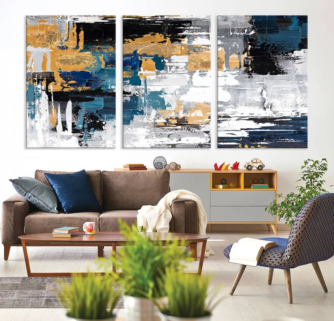 The Blue and Gold Abstract Canvas Wall Art – a triptych modern painting that's framed and ready to hang – features captivating brush strokes in blue, gold, black, and white to enhance the living room decor.