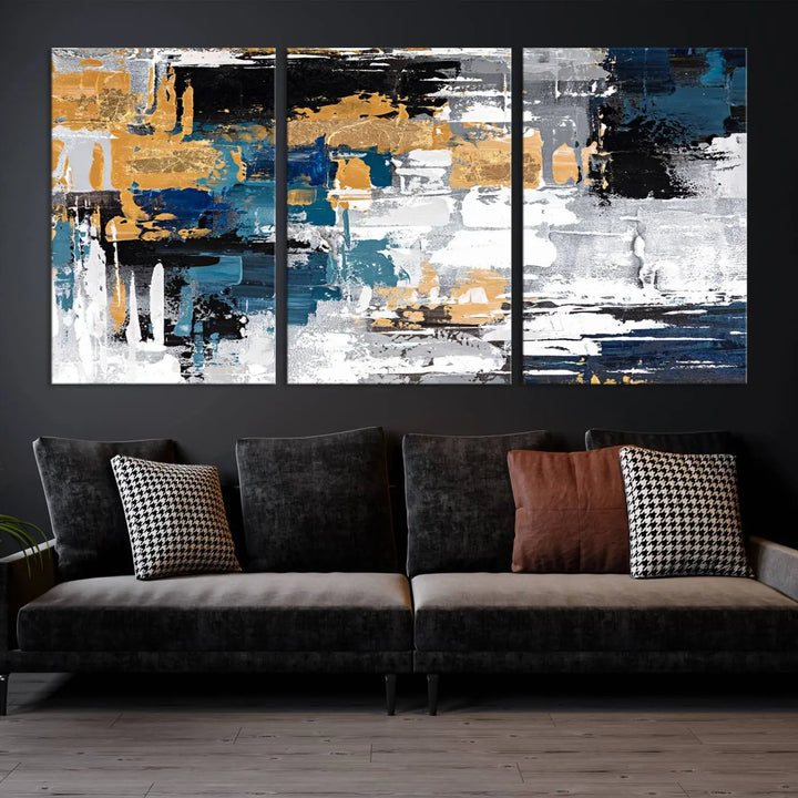 The Blue and Gold Abstract Canvas Wall Art – a triptych modern painting that's framed and ready to hang – features captivating brush strokes in blue, gold, black, and white to enhance the living room decor.