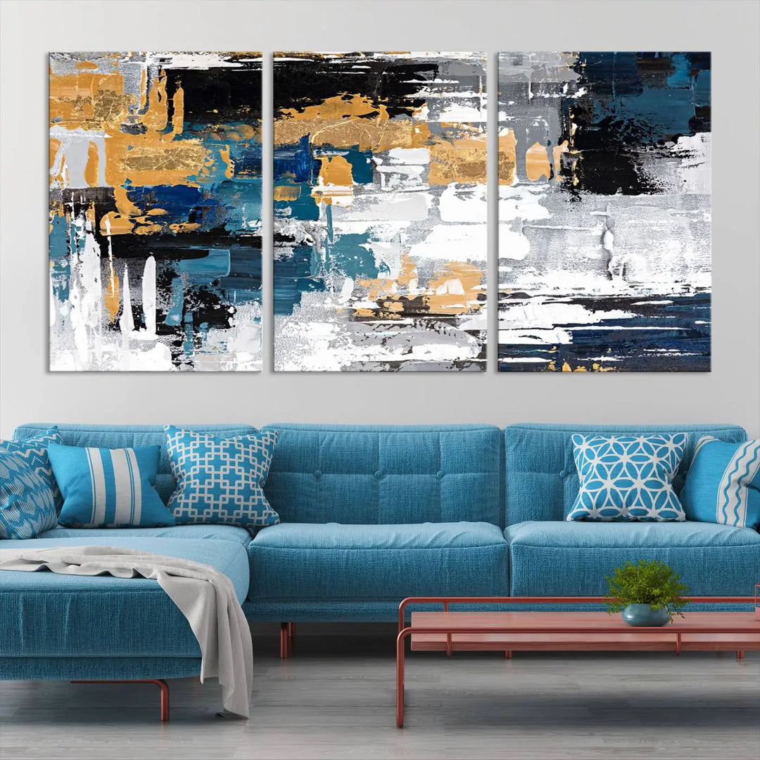 The Blue and Gold Abstract Canvas Wall Art – a triptych modern painting that's framed and ready to hang – features captivating brush strokes in blue, gold, black, and white to enhance the living room decor.