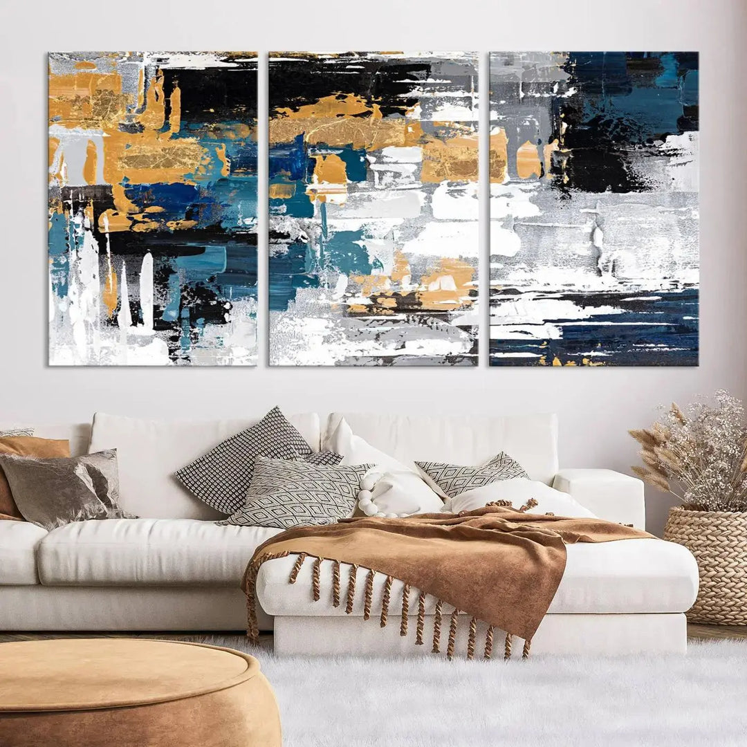 The Blue and Gold Abstract Canvas Wall Art – a triptych modern painting that's framed and ready to hang – features captivating brush strokes in blue, gold, black, and white to enhance the living room decor.